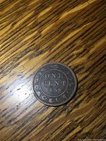 Obverse side of 1859 Canada One Cent coin showing 'ONE CENT 1859' with floral border on wooden background