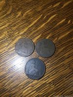 Three large antique pennies displayed on a wooden surface, showing the circulated wear and patina.