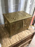 Full view of rectangular vintage brass ash box with ornate embossed texture, lion paw feet on wooden surface.