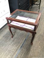 Front angle view showing wood frame, glass top and sides, patterned lining inside, and cabriole legs.