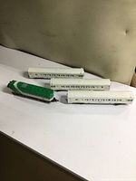 Photo showing green and white locomotive with three white passenger cars on a white surface.