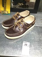 Side angle showing brown leather shoe with beige lining and cream sole, leather lace tied in bow on top.