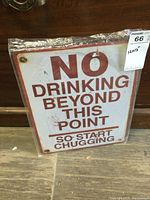 Full front view of the metal sign showing the text 'NO DRINKING BEYOND THIS POINT SO START CHUGGING' with some light weathering and four mounting holes.