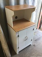 Front view of microwave stand showing wood top, open shelf with cable access hole, and white cupboard with two doors and silver handles