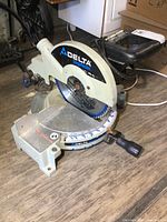 Front and side view of Delta ShopMaster 10-inch miter saw with circular saw blade and handle visible.