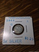 Obverse side of the 1944 Newfoundland 5 cent silver coin in holder showing coin and printed labeling with price and date.