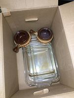 Top-down image capturing three transparent Pyrex glass baking dishes stacked inside a cardboard box, showing clear glass with integrated handles.