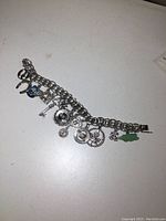 Full view of the silver charm bracelet with all 14 charms laid out on a white surface.