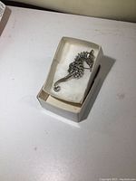 Sterling silver vintage seahorse brooch shown in a white box with soft cushioning, viewed from above.