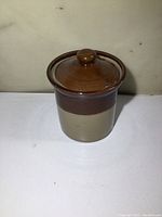 Side view of the small stoneware crock showing two-tone color and lid with knob handle.