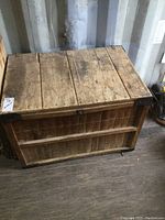 Front view of the vintage wooden crate showing hinged lid, natural wood worn surface, and metal corner braces.