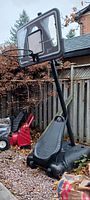 Outdoor adjustable basketball hoop with clear plastic backboard and black rim. Weighted base visible filled with material for stability.