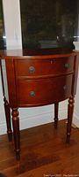 Front view of the Bowring wooden bedside table showing curved front, turn legs, and drawer handles.