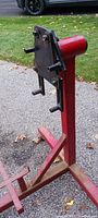Red metal engine stand photographed outdoors on pavement, showing front mounting plate and support base from multiple angles.