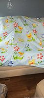 Fabric spread out on a couch showing playful children's design with yellow chicks, colorful flowers, and grass on a light blue background.