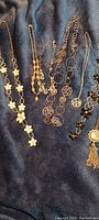 Several gold-tone fashion necklaces displayed on dark fabric showing floral and bead details.