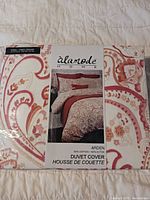 Photo of packaged king size duvet cover with red and peach paisley floral design and product label showing brand Alamode Home and Arden pattern