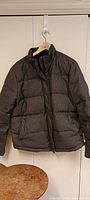 Front view of the dark grey speckled down winter coat on a hanger showing front zipper and pocket details.