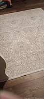 Full view of the rectangular off white rug with taupe floral and geometric pattern on wooden floor