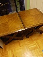 Pair of wooden side or end tables with matching square tops and decorative curved and carved legs shown together on wood flooring.