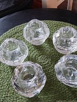 Top-down view of five clear textured glass candle holders with snowball-like design arranged on a surface.