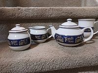 Full view of Tetley Teas porcelain tea set including teapot, sugar bowl, creamer, and mug arranged on carpeted stairs.
