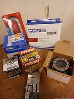 Box of new unused car parts including Fram oil filters, Wix filters, Delphi Technologies automotive part, and a radio replacement interface.