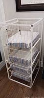 Full view of the front and side of the white metal wire storage unit with four drawers and fabric liners, showing size and overall condition.