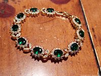 Close-up of bracelet showing emerald green oval glass stones and clear crystals with gold plated setting.