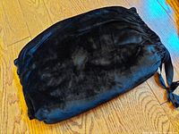Black velvet hand muff laid flat on wooden floor, showing exterior texture and size