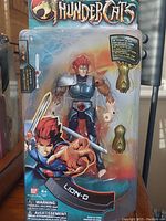 Front view of sealed Lion-O action figure in blister pack, showing figure, sword accessory, and interchangeable hands inside the package.