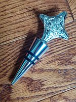Silver plated wine stopper with detailed Haida art design, rubber rings on tapered shaft for sealing bottles.