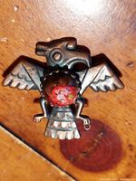 Top-down view of the copper raven pendant/brooch showing detailed wings, bird head, and round reddish centerpiece.