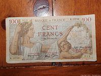 Front side of the 1940 Banque De France 100 Francs Sully Type 1939 banknote placed on a wooden surface, showing details of the allegorical woman and child, signatures, serial numbers, and inscriptions.