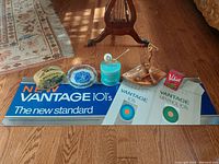 Wide shot of tobacco collectibles including tins, pipe container, and advertising signage displayed on wooden floor.