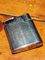 Angled top-down photo of the vintage Ronson lighter showing front with vertical striped metal surface and details at the top mechanism and bottom stamping.