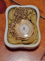 Front view of two-sided pendant watch with gold-textured circular surround and white dial marked Norman.