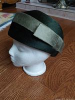 Side angle profile of the vintage Edna Wallace hat on a white mannequin head on a wooden floor.