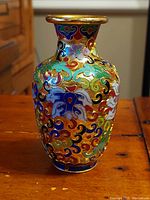 Front view showing detailed multicolored floral patterns on cloisonne vase with gold rim
