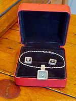 Boxed set of a sterling silver bracelet and matching earrings with square blue-green stones and small gemstone accents.