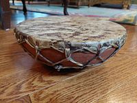 Side view of vintage handcrafted drum showing circular hide stretched over terracotta base with leather lacing.