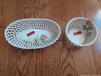 Two vintage hand woven porcelain baskets by Janusz Baranowski with pink porcelain roses, placed on wooden surface