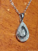 Close-up front view of the teardrop pendant showing the clear and black gemstones and swirling pattern.