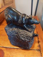 Side view showing the black stone bear sculpture crouching on a textured stone base