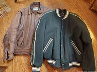 Two vintage men's bomber style jackets laid flat on wooden floor, one brown leather and one black wool with leather detailing