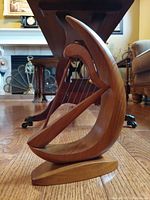 Side angle of handcrafted wooden harp sculpture showing curved crescent frame, wood strings, triangular support beam, and oval base