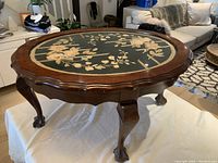 Full view of the oval walnut coffee table showing the floral fabric inlay protected by glass and the carved claw feet.