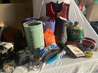 Photo of camping gear items including sleeping pads, pillow, stove, fuel bottle, sleeping bag and accessories laid out on white surface