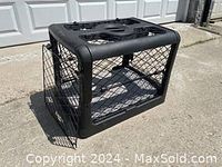 Full side view of the charcoal black collapsible dog crate with open front door sitting on concrete.
