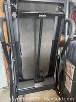 Electric treadmill folded vertically showing black and grey metal frame and running belt underside.